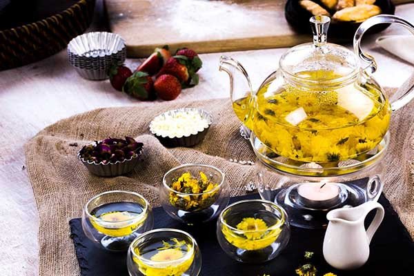 Ấm trà thủy tinh trong suốt với những bông hoa cúc đang nở bung, cho thấy tính thẩm mỹ khi pha trà hoa cúc