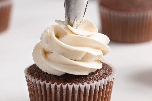 Bàn tay đang trang trí kem tươi lên bánh cupcake socola với túi bắt kem.
