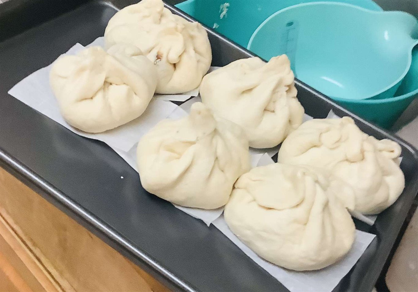 Bánh bao được đặt trên giấy nến trong lòng nồi chiên không dầu, chờ hấp để có độ mềm ngon
