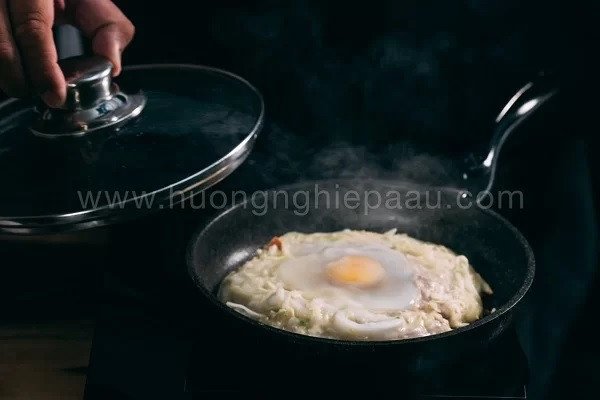 Chiên bánh Okonomiyaki trên chảo nóng, thêm trứng gà và đợi bánh chín vàng
