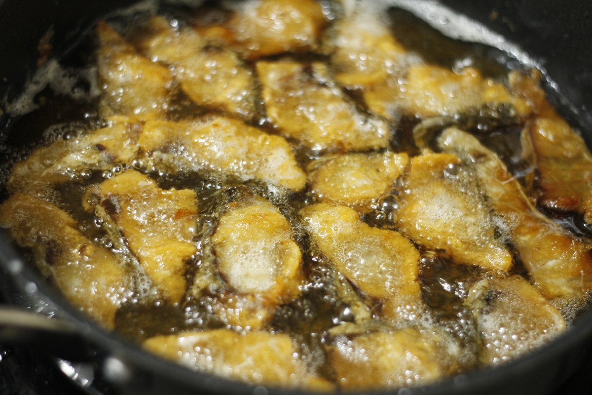 Đầu bếp đang lật mặt miếng cá tẩm bột chiên giòn trong chảo dầu nóng.