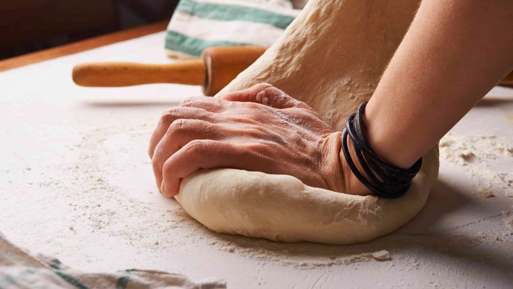 Khối bột bánh mì cuộn len đang được nhào trộn đều trên mặt phẳng sạch