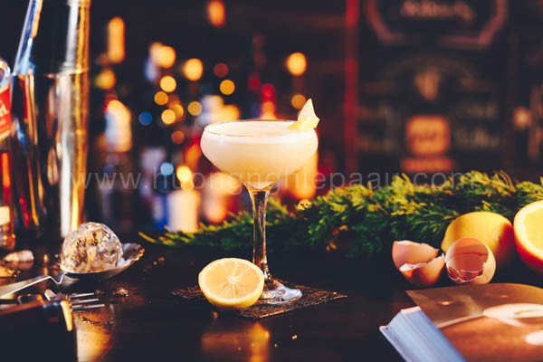 Ly cocktail Whisky Sour vàng hổ phách với bọt trắng mịn, trang trí lát cam khô và cherry, minh họa sự pha chế độc đáo
