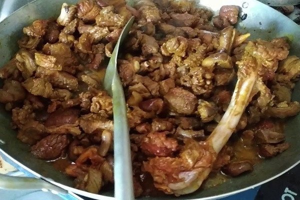 Người đầu bếp đang xào thịt chó trong chảo gang lớn với nhiệt độ cao, tạo ra món thịt chó xào lăn vàng ươm hấp dẫn.