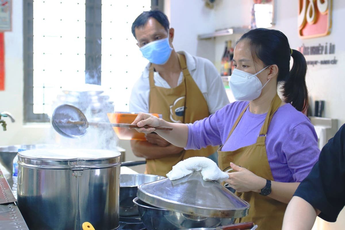 Bí Quyết Làm Bánh Cuốn Nóng Và Bánh Ướt Lòng Gà Ngon Chuẩn Vị Người làm bánh đang tráng bánh cuốn nóng trên bếp hấp, khói bay nghi ngút