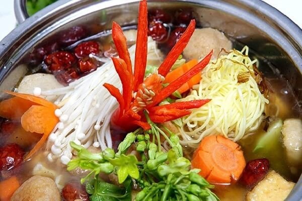 Nồi lẩu nấm chay chua cay bốc khói nghi ngút, nước lẩu đỏ cam hấp dẫn, bên trong là các loại nấm tươi ngon và rau xanh.