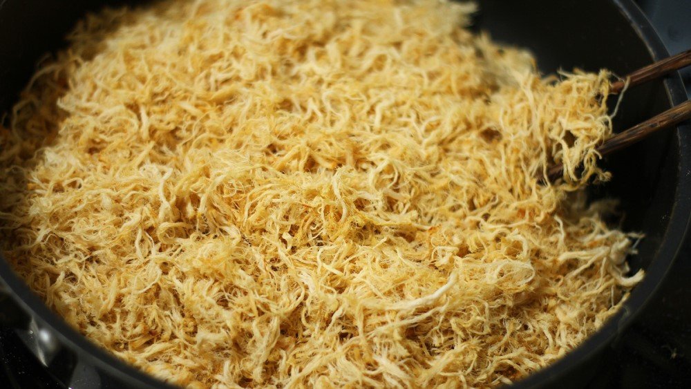 Ruốc thịt heo đang được sao khô trên chảo với lửa nhỏ, đảm bảo sợi ruốc bông đều và có màu vàng đẹp mắt.