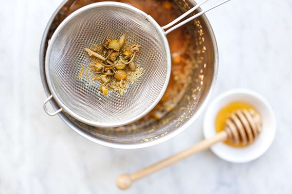 Sử dụng rây lọc để loại bỏ bã sau khi pha trà hoa cúc cam thảo, đảm bảo nước trà trong vắt