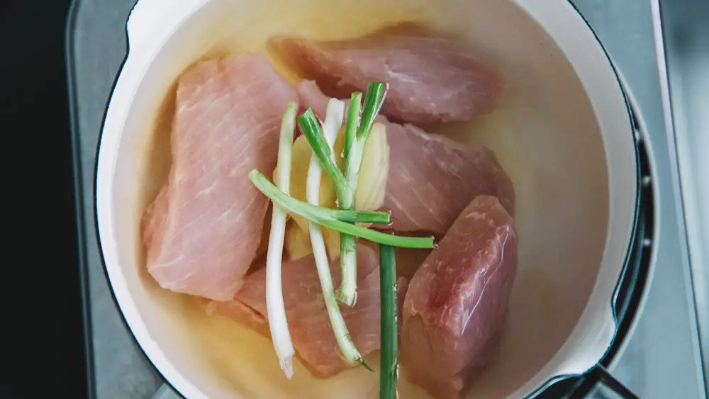 Thịt heo đang được luộc trong nồi với các loại gia vị như nước mắm, tiêu, hành tây để thấm đều hương vị làm ruốc.