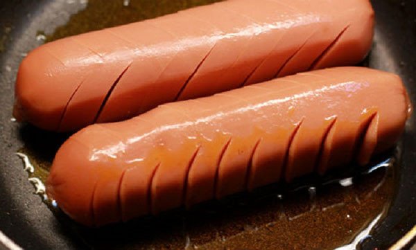 Xúc xích chiên vàng giòn trên chảo nóng để làm bánh mì chảo thơm ngon