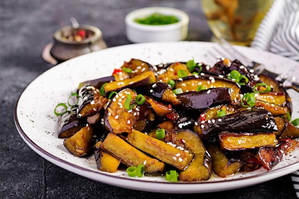 Bàn tay đang chọn những quả cà tím tươi ngon, có vỏ bóng và cuống xanh.