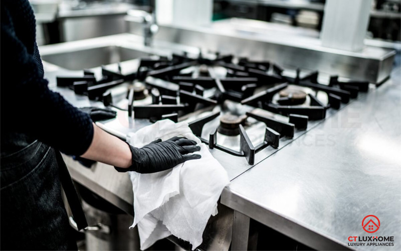 Bàn tay đang kiểm tra van điều chỉnh của bếp ga, phía dưới là bình gas và ống dẫn gas.