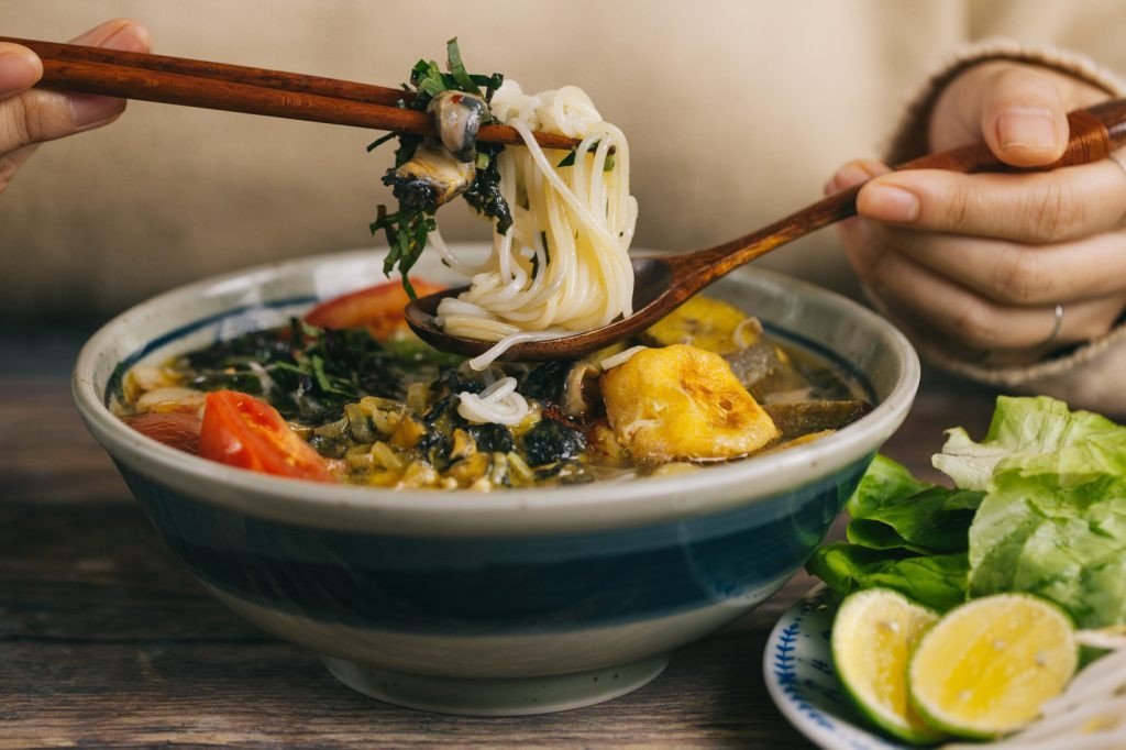 Bát bún ốc chuối đậu nóng hổi, đầy đặn với ốc, chuối xanh và đậu phụ chiên, tô điểm rau thơm và ớt chưng, sẵn sàng thưởng thức