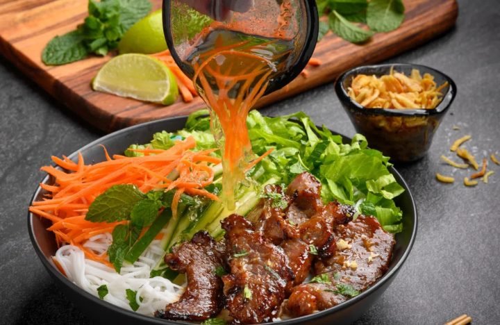 Bát bún thịt nướng đầy đủ topping, rau sống và nước chấm.