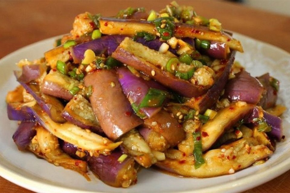 Cà tím đang được xào trên chảo cùng với các loại gia vị tạo màu sắc hấp dẫn