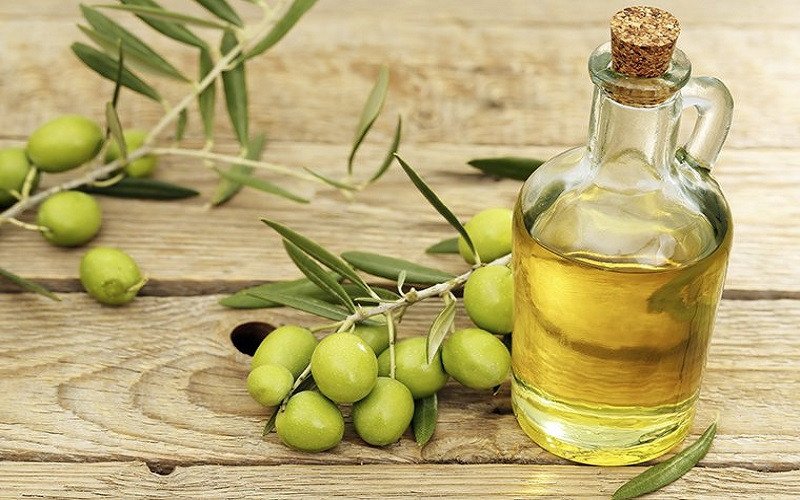 Chai dầu ô liu nguyên chất đặt cạnh những quả ô liu tươi, nhấn mạnh nguồn gốc tự nhiên của loại dầu này.