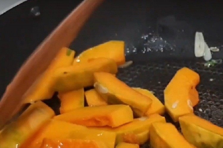 Chảo bí đỏ xào tỏi đang được đảo đều trên bếp lửa