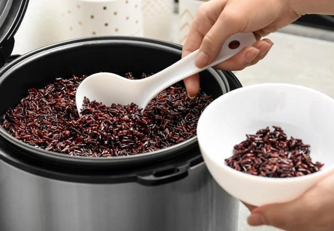 Cơm gạo lứt huyết rồng đang được nấu chín trong nồi cơm điện, toả hương thơm nhẹ nhàng