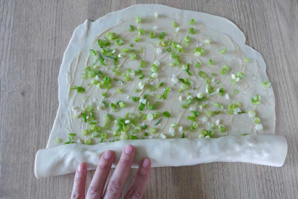 Cuộn bột hành lá đã phết nhân, bước quan trọng để bánh hành chiên có nhiều lớp giòn.
