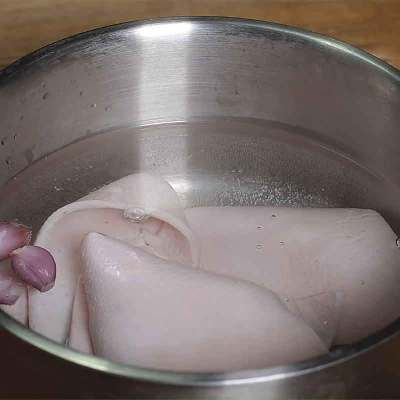 Da lợn đang được luộc trong nồi nước sôi với hành tím.