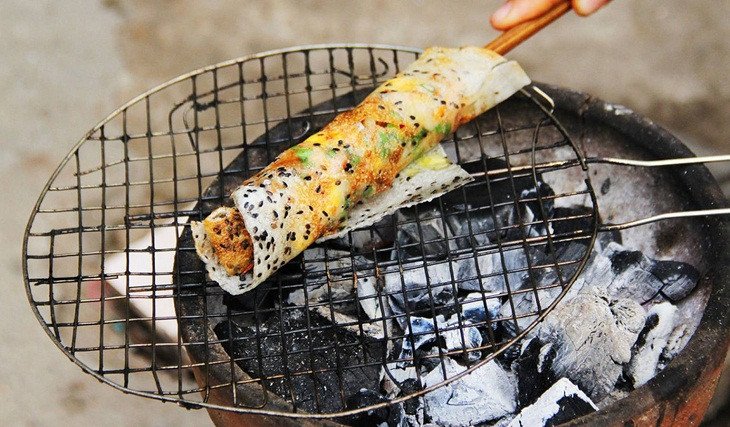 Đặt bánh tráng lên bếp than hồng, thêm các nguyên liệu nhân và trứng để nướng bánh tráng mắm ruốc truyền thống