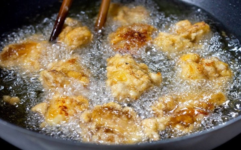 Đầu bếp đang chiên rán món ăn trong chảo với dầu ăn, tượng trưng cho việc sử dụng chất béo trong các món chiên xào.