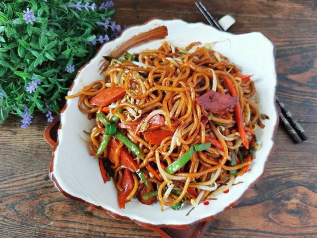 Đĩa mì gạo xào thập cẩm đầy màu sắc với rau củ, xúc xích và sợi mì tơi ngon, không dính.