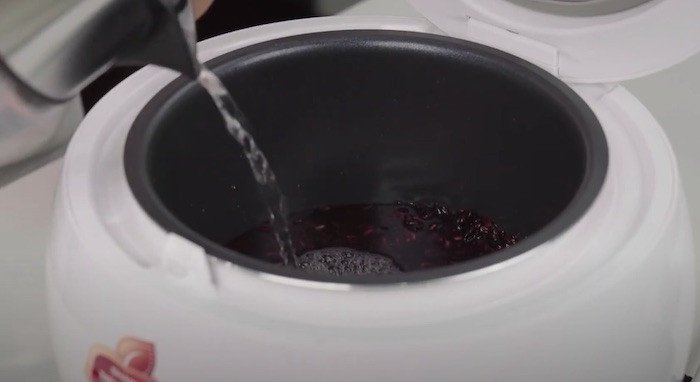 Đong nước và thêm gia vị vào nếp cẩm để nấu bằng nồi cơm điện