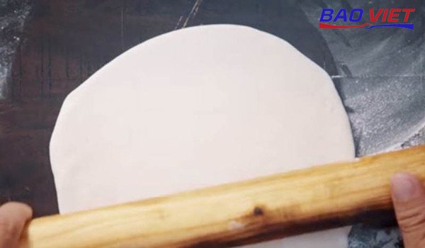Dùng cây cán bột làm dẹt khối bột mì đa dụng thành miếng mỏng đều để chuẩn bị làm vỏ bánh bao chay
