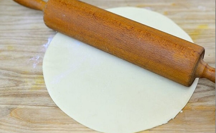 Dùng cây cán gỗ để cán mỏng từng miếng bột, tạo hình vỏ bánh sủi cảo đều và đẹp mắt.