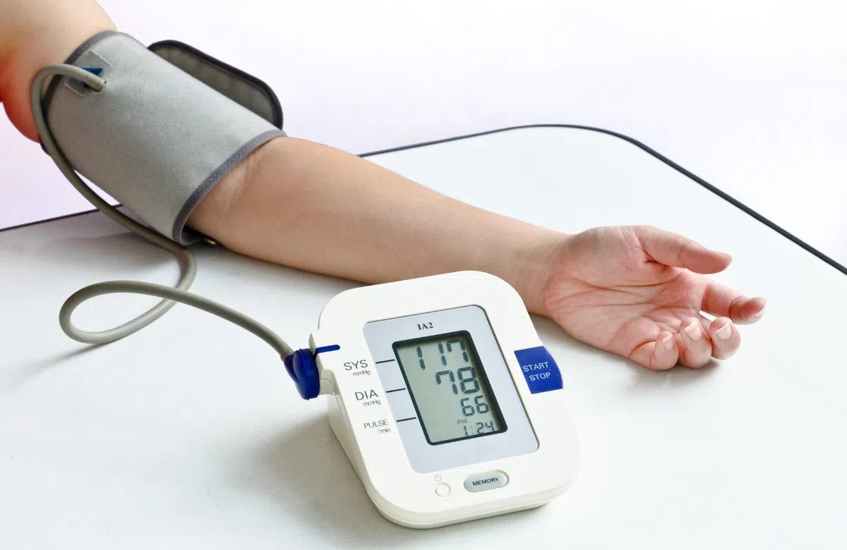 Hình ảnh một người phụ nữ đang kiểm tra huyết áp bằng máy đo, với lá ổi tươi và ly nước lá ổi trong khung cảnh, minh họa cho việc nước lá ổi có thể ảnh hưởng đến huyết áp