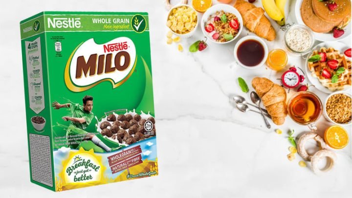 Hộp ngũ cốc Milo dinh dưỡng đặt trên bàn ăn sáng cùng trái cây tươi ngon, tượng trưng cho bữa ăn đầy năng lượng.