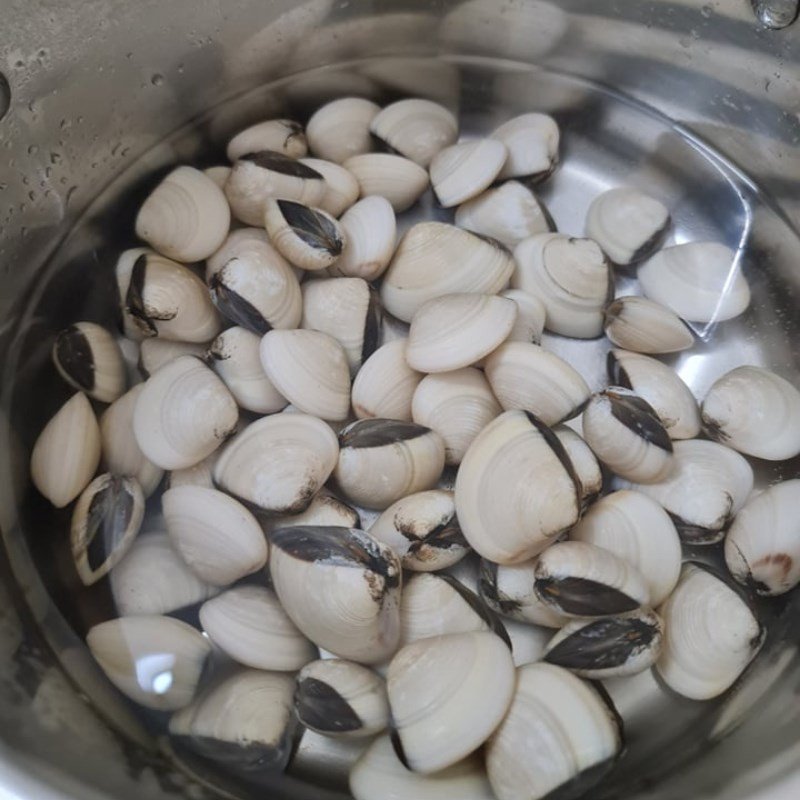 Lọc nước luộc ngao qua rây để loại bỏ cặn, chuẩn bị nước dùng cho canh ngao dứa cà chua