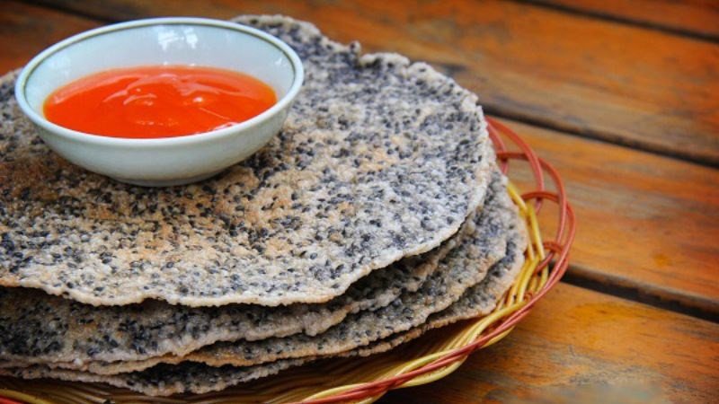 Một chiếc bánh đa vừng giòn được chấm vào chén tương ớt đỏ tươi, thể hiện món ăn vặt đơn giản và ít calo