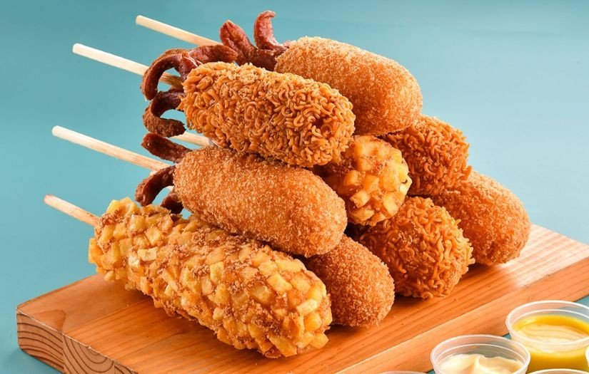 Một chiếc hotdog với đầy đủ topping như hành tây, dưa chuột và sốt, được cầm trên tay thể hiện sự tiện lợi của đồ ăn nhanh