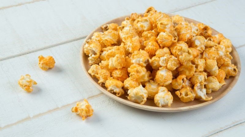 Một phần bắp rang bơ với các lớp phủ phô mai hoặc caramel bắt mắt, minh họa cho những loại bắp rang bơ giàu calo cần hạn chế nếu muốn kiểm soát cân nặng.