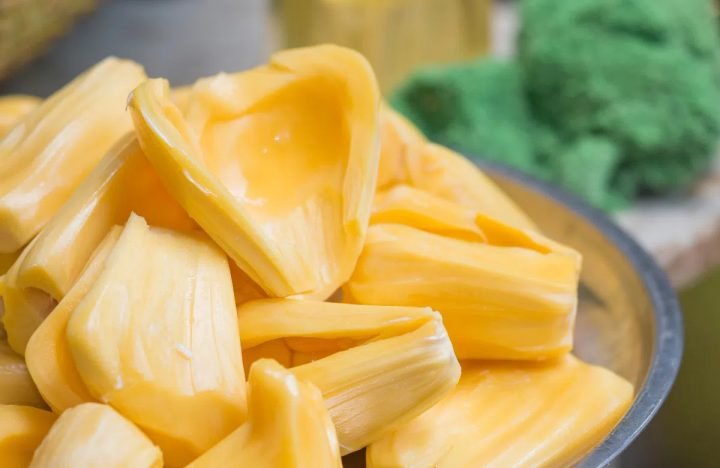 Một phụ nữ đang thưởng thức múi mít ướt tươi ngon, thể hiện niềm vui và sự hài lòng với hương vị tự nhiên của quả mít.