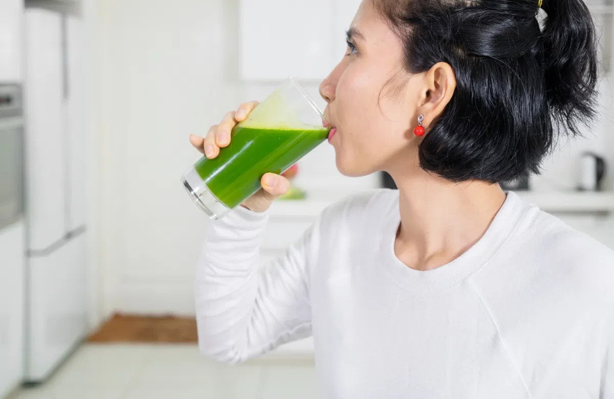 Người phụ nữ cầm ly nước rau diếp cá xanh tươi