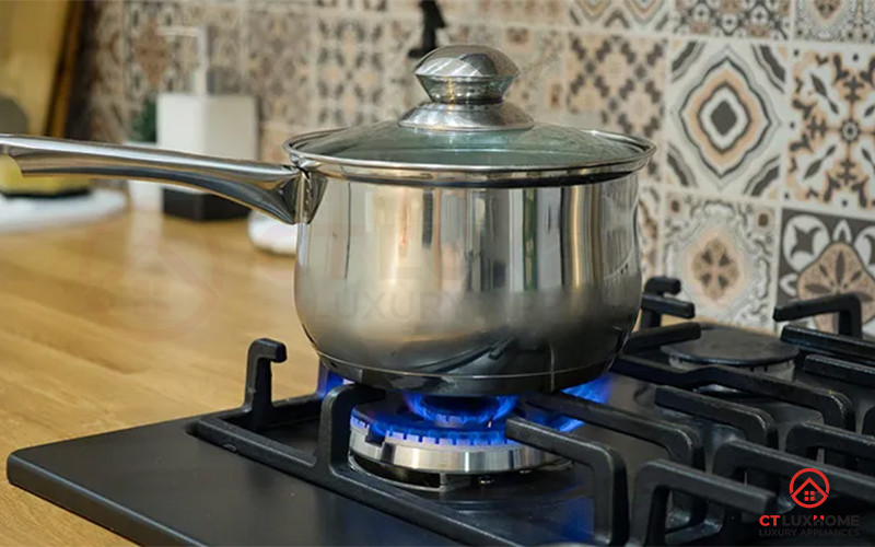 Người phụ nữ đang cẩn thận khuấy nồi cháo sôi trên bếp ga, xung quanh khu vực bếp sạch sẽ.