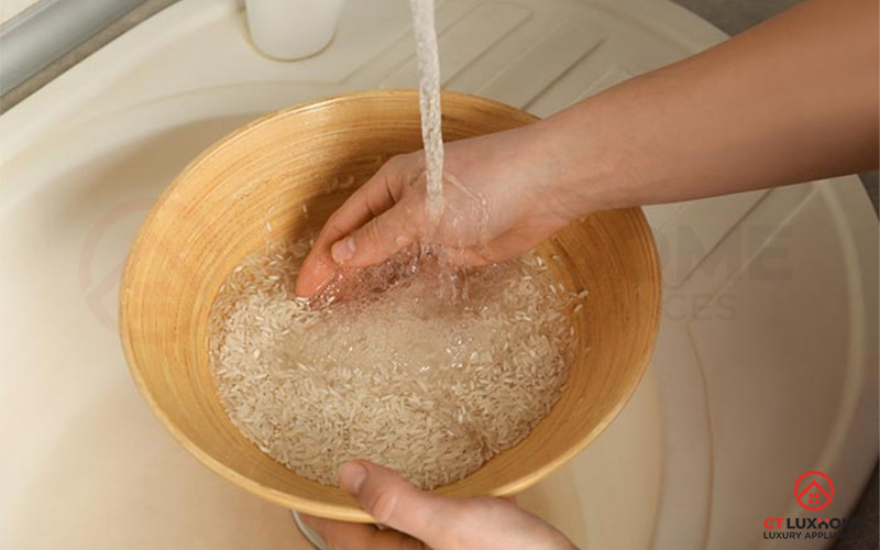 Người phụ nữ đang vo gạo trong một cái rổ lớn dưới vòi nước chảy.