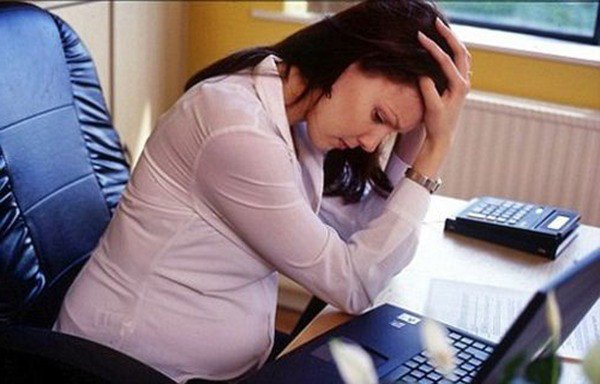 Người phụ nữ làm việc văn phòng đang ngồi trên ghế và cầm bụng của mình, thể hiện sự tích tụ mỡ bụng dưới.