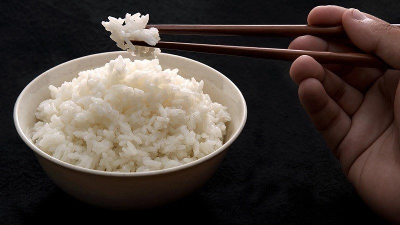 Người phụ nữ vui vẻ ăn cơm cùng rau củ, minh họa việc ăn uống cân đối để không lo tăng cân.