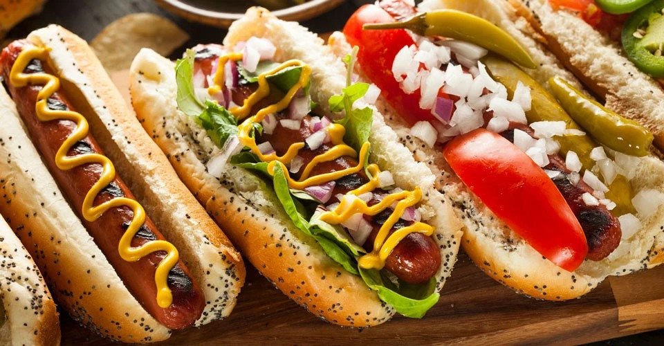 Nhiều chiếc hotdog đang được chiên vàng trên chảo dầu nóng, thể hiện quá trình chế biến món ăn vặt phổ biến và tác động của dầu chiên đến lượng calo