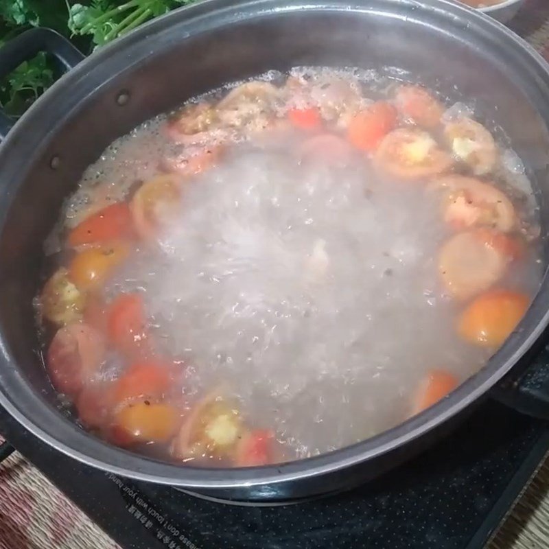 Nhúng rau thì là và các loại rau ăn kèm vào nồi lẩu cá trắm nóng hổi.