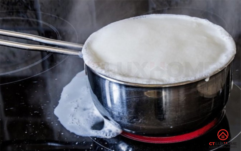 Nồi cháo đang sôi nhẹ trên bếp ga, có một chiếc thìa gỗ đặt ngang miệng nồi để chống trào.