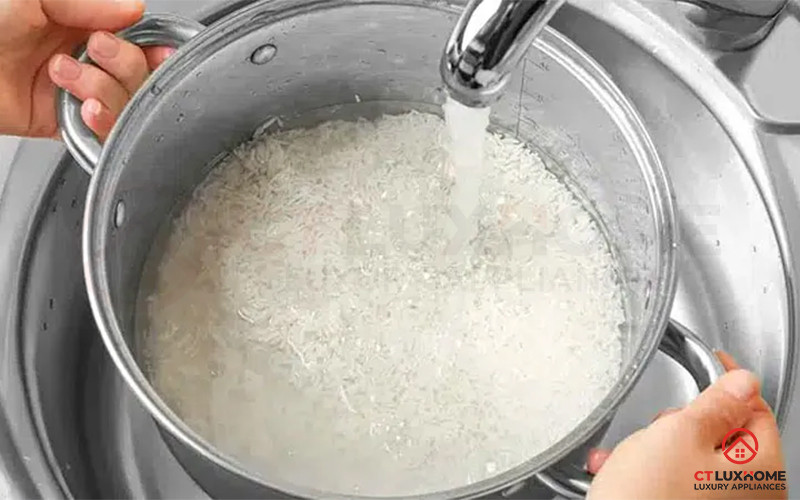 Nước đang được đổ vào nồi có gạo, một người phụ nữ đang cầm thìa gia vị.