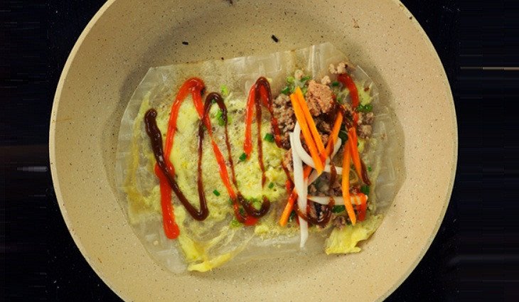 Phết bơ, đập trứng cút và dàn đều các loại nhân như pate, thịt băm, mắm ruốc lên bánh tráng trên chảo chống dính