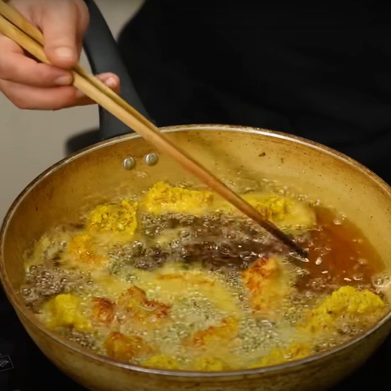 Thịt lợn chiên riềng vàng đều, giòn tan đang được vớt ra khỏi chảo