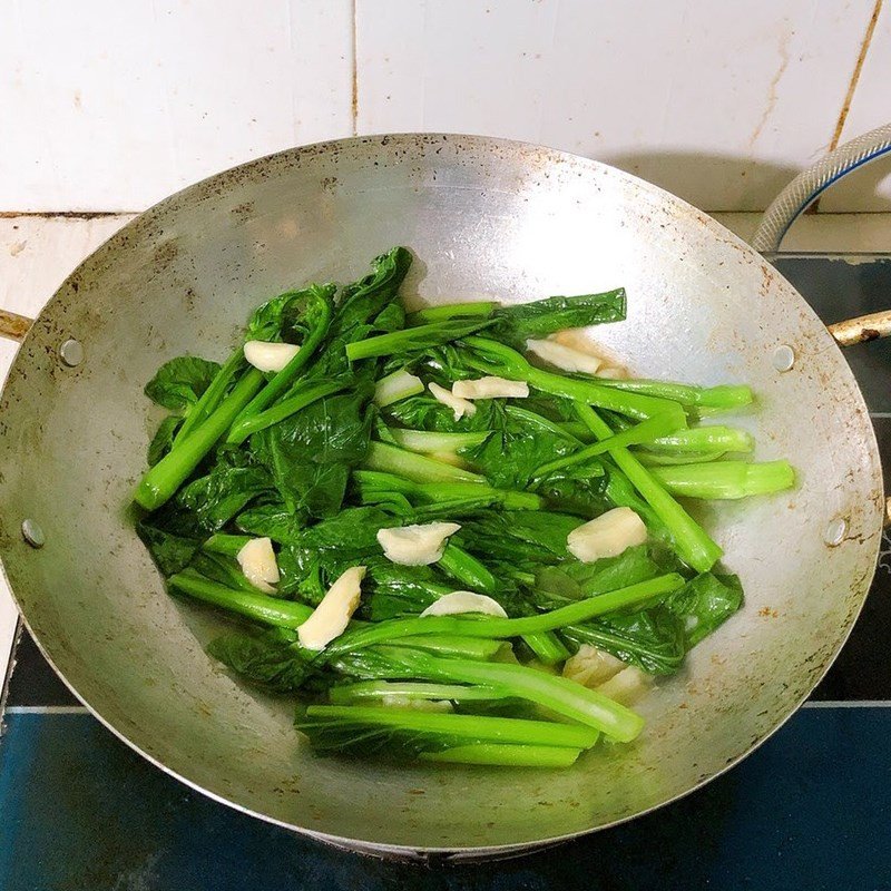 Đảo đều cải ngồng trong chảo để rau chín đều và ngấm gia vị